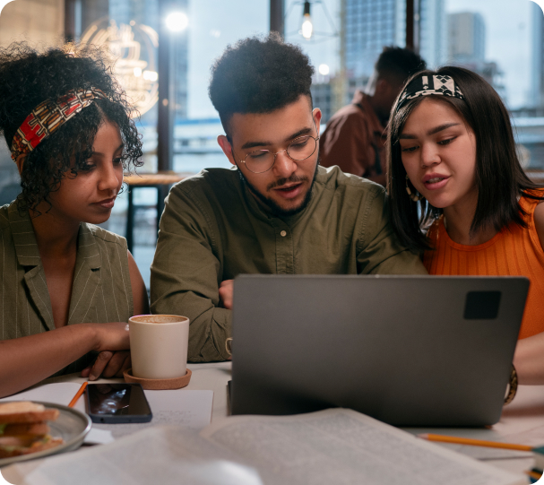 Two girls and a guy are discussing something while looking at a laptop.